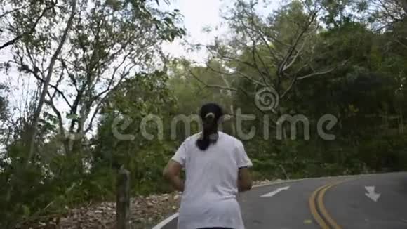 亚洲女人在路上穿过小山从女性跑步者的后侧看向山视频的预览图