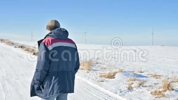 一个穿着帽子和温暖夹克的和夹克的沉思的男子在一个阳光明媚的冬天在一个室外的田野里看到一幅风景视频的预览图