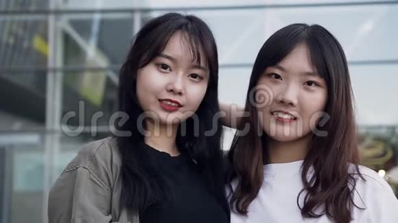 两个微笑可爱的亚洲女孩的漂亮肖像手里拿着购物袋看着大商店附近的摄像机视频的预览图