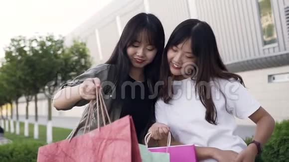 两位迷人无忧无虑的亚洲女性最好的朋友站在购物中心的墙边展示报纸上的内容视频的预览图