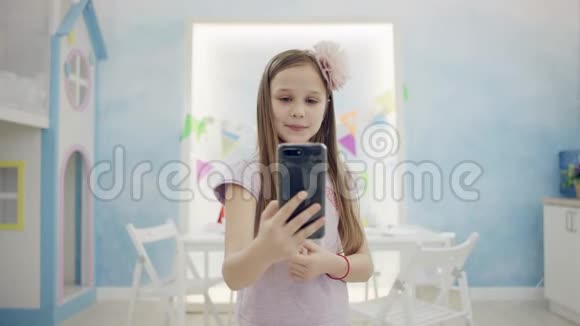 小女孩用智能手机站在房间里的摄像机前在视频聊天中聊天视频的预览图
