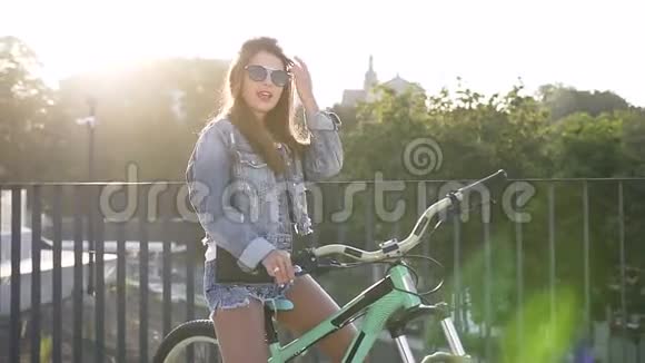 美丽的女人的肖像留着长发穿着时尚牛仔裤坐在自行车上用相机唱歌跳舞视频的预览图