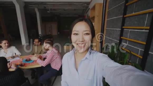 在现代办公室工作的同事中一位拥有智能手机的开朗的亚洲女性可以通过现场视频通话视频的预览图