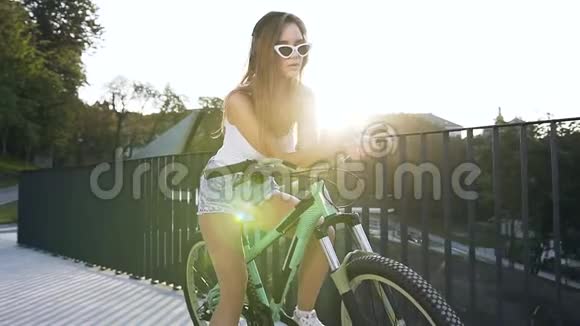 年轻的白种人戴着时髦的太阳镜长发坐在自行车上通过耳机听音乐视频的预览图