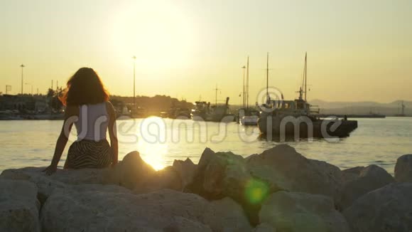 傍晚海上港口日落时游客女孩在石上日落美景中的女人视频的预览图