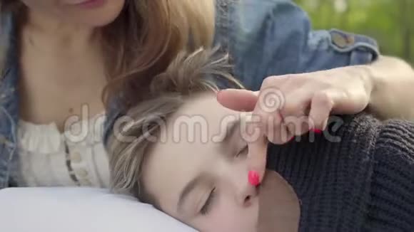 肖像漂亮的男孩睡在妈妈手里女人在公园里抚摸她孩子的头发户外休闲视频的预览图