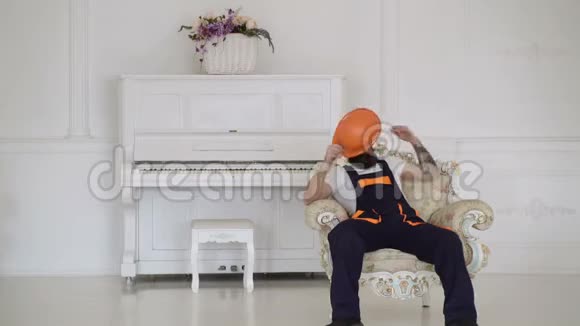 疲惫的装载机坐在扶手椅上休息时被隔离在白色上钢琴背景孤立在白色上昂贵的内部视频的预览图
