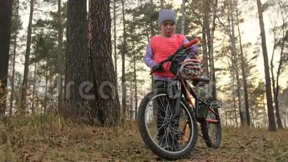 孩子戴头盔一个高加索儿童在秋季公园骑自行车在森林里骑着黑色橙色自行车的小女孩视频的预览图