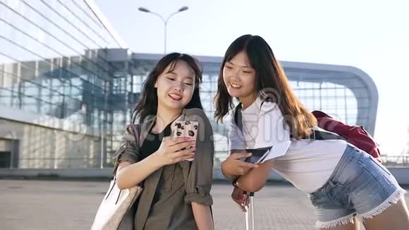 迷人的25岁亚洲女性旅客站在现代机场附近使用智能手机视频的预览图
