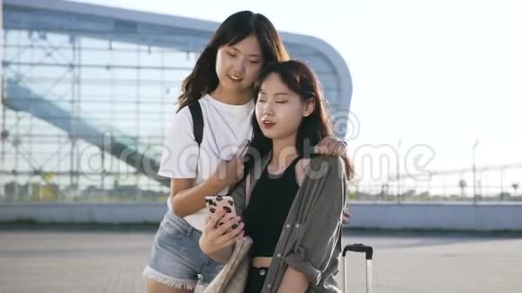 美丽的25岁亚洲女孩留着长发看着电话微笑着靠近现代机场大楼视频的预览图