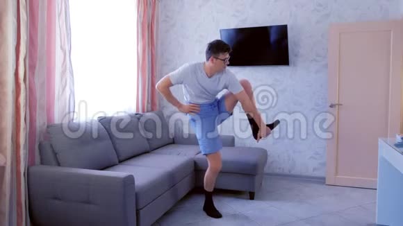 有趣的书呆子正在做腿部伸展运动试图抬起他的腿然后在家里摔倒在地板上视频的预览图
