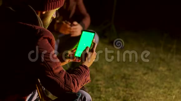 游客在篝火旁用绿色的屏幕在电话上嘲笑视频的预览图
