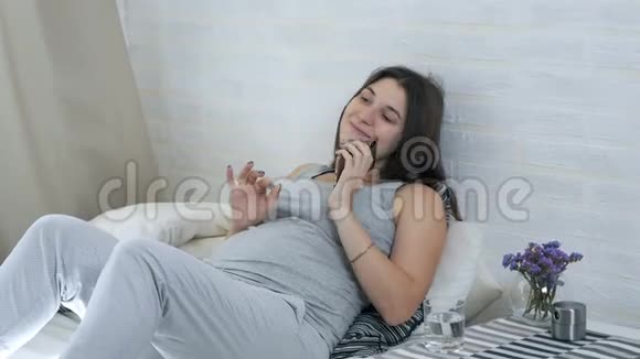 一个年轻的怀孕女孩躺在沙发上用手机说话孕妇的休闲视频的预览图