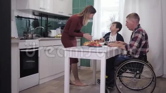 快乐的父母残疾的父亲在为家人做饭的时候与慈爱的妻子和快乐的儿子一起玩视频的预览图