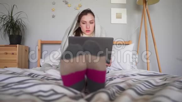可爱的女孩用毯子盖上被子想着生意看着笔记本屏幕穿睡衣的女人视频的预览图