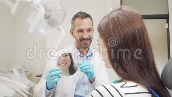一位成熟开朗的牙医为他的女病人拿着镜子视频的预览图
