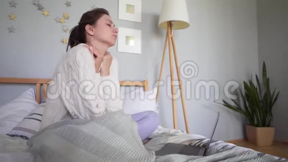 漂亮的白种人女人又累又冷穿着舒适的格子衣服在笔记本电脑屏幕上学习文件视频的预览图