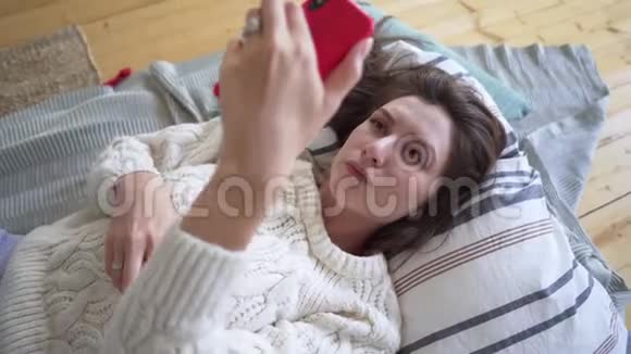 一位穿着白色毛衣的漂亮女士躺在毯子上用面部和眼睛识别进行网上购买视频的预览图