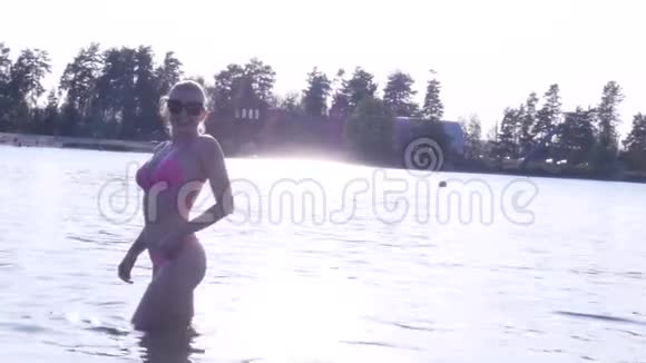 穿比基尼的性感金发女孩在日落时进入湖中视频的预览图