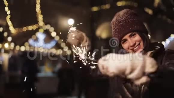 穿着冬装的漂亮微笑的女孩高兴地看着镜头拿着火花旋转和跳舞站在里面视频的预览图