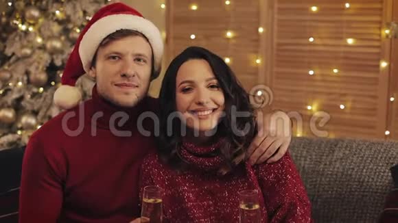 在温暖舒适的家庭氛围中一对幸福微笑的情侣坐在圣诞树旁手捧眼镜视频的预览图