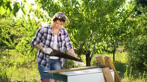 漂亮的女木匠在阳光明媚的果园里看着相机和手锯木板视频的预览图