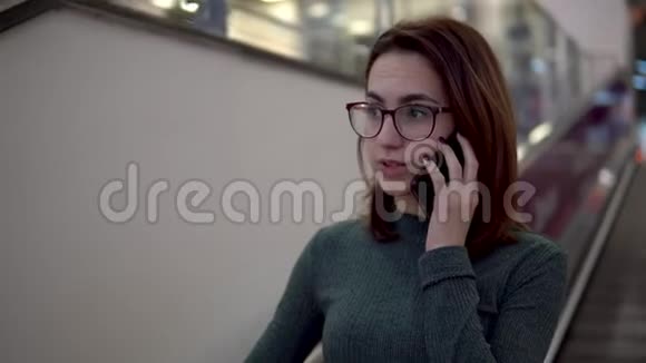 一个年轻的女人坐在自动扶梯上打电话大型购物中心视频的预览图