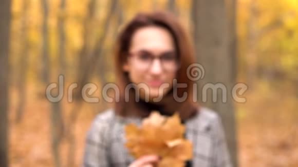 一个戴眼镜的年轻女人躲在秋天森林里的一棵大树叶子后面女孩伸出叶子对着镜头视频的预览图