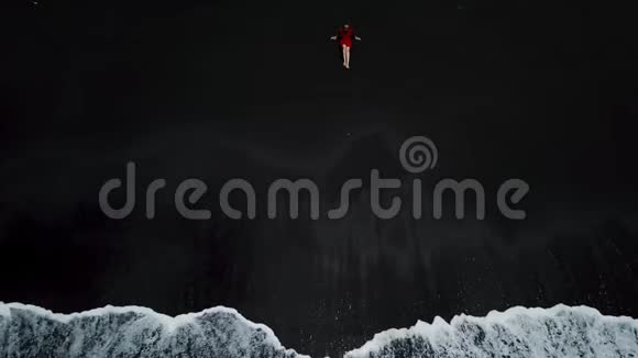 鸟瞰一个穿着红色连衣裙的女孩坐在海滩上沙滩上有黑色的沙子西班牙加那利群岛特内里费视频的预览图
