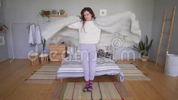 穿着睡衣和毛衣的漂亮年轻女子正在床边跳舞玩得很开心躲在毯子里视频的预览图