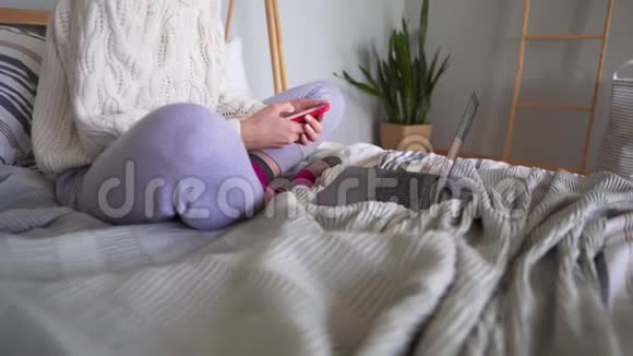 特写一个女人用手机和笔记本电脑在家工作穿着睡衣躺在床上的自由职业者视频的预览图