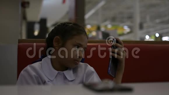 亚洲可爱的女学生坐在自助餐厅用手机视频的预览图