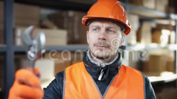与面包和胡子工人一起工作戴着头盔和工作服站在架子旁边检查一个可调节的扳手视频的预览图