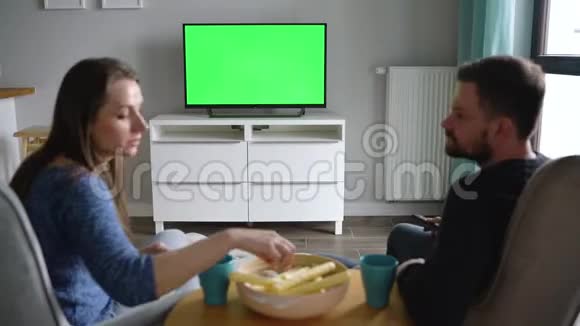 男人和女人坐在椅子上用绿色的屏幕看电视喝茶吃零食和说话后景铬视频的预览图