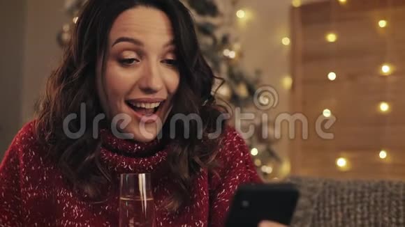 年轻美丽的女士用手机端着一杯香槟微笑着坐在附近视频的预览图