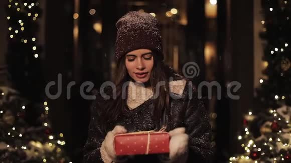 快乐的微笑美丽的女人在冬天的衣服拥抱红色的礼物盒猜猜里面是什么看镜头的女孩视频的预览图