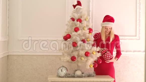 在白色墙上拿着圣诞礼物盒的圣诞老人性感女人室内模特儿时尚画像视频的预览图