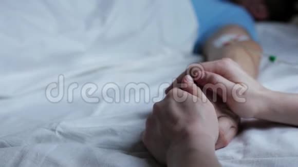 男人手拿着滴管在医院的床上睡觉女人握着他的手视频的预览图