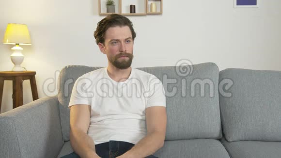 无聊的男人独自坐在房间里的沙发上看电视手里拿着遥控器切换频道视频的预览图