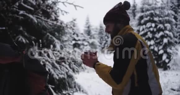 在寒冷的冬天独自旅行的年轻人他停在雪林中喝了些热饮料视频的预览图
