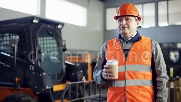 戴着头盔和工作服的导演站在新的工作设备旁边对着镜头喝咖啡视频的预览图