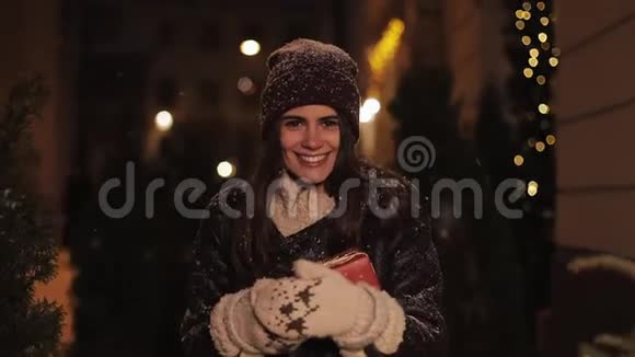 穿着冬衣看着幸福捧着礼盒走在落雪中的微笑少女的画像视频的预览图
