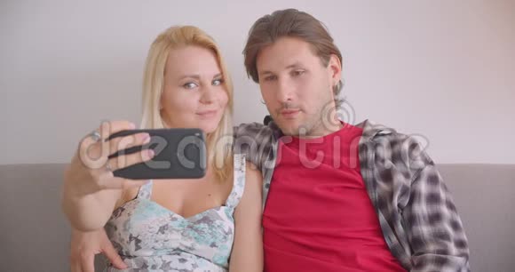 一对有魅力的白种人夫妇在电话中自拍幸福地坐在室内沙发上微笑视频的预览图