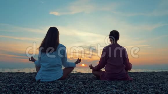 两位年轻女性在日落时在海边或海洋练习瑜伽视频的预览图
