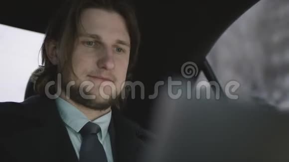 穿着开心果衬衫和灰色外套的棕色头发的帅哥坐在车里用他的平板电脑视频的预览图