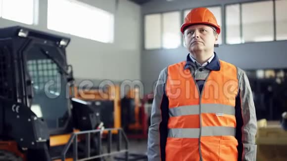 戴着头盔和工作服的主任站在新的工作设备旁边看着另一个工人的镜头视频的预览图