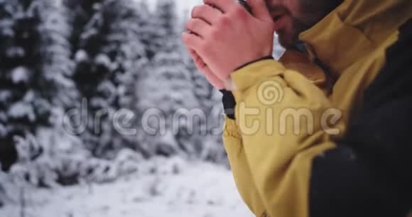 一位身穿黄色夹克衫的游客在寒冷的冬日在白雪森林中冻僵了他拿起一个铁杯视频的预览图