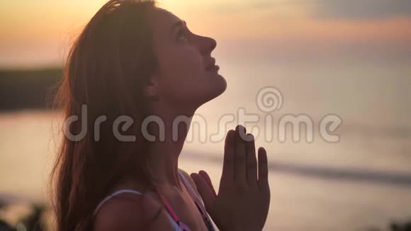 美丽的女孩祈祷仰望橙色的天空与希望特写年轻女子梦中的剪影视频的预览图