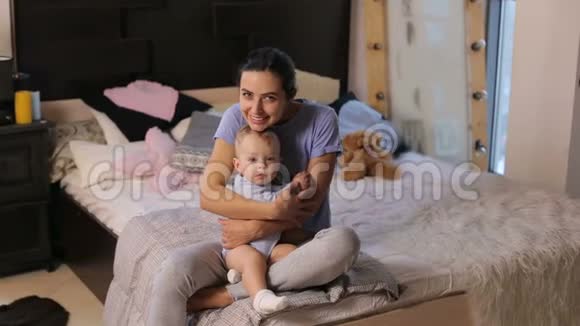 一位可爱的年轻母亲在舒适的卧室里拥抱她的小儿子的肖像视频的预览图