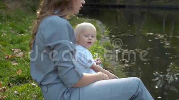 一位年轻的母亲和她蹒跚学步的孩子坐在湖边视频的预览图